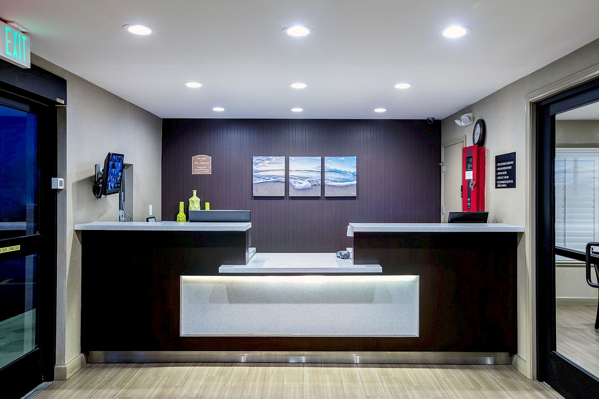 A hotel lobby with a reception desk, TV, artwork, fire extinguisher, and clock.