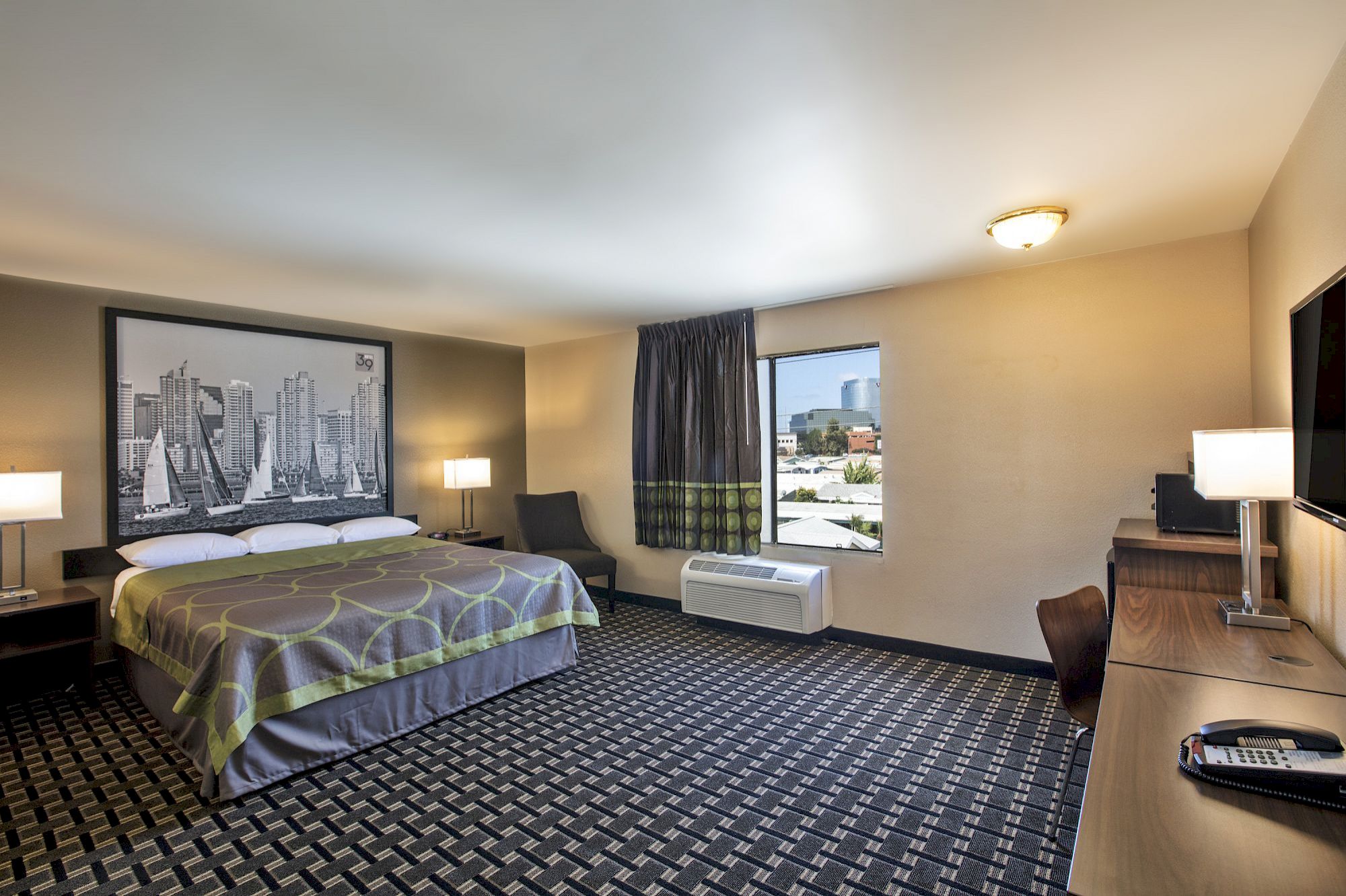 A hotel room with a bed, desk, window, and TV.